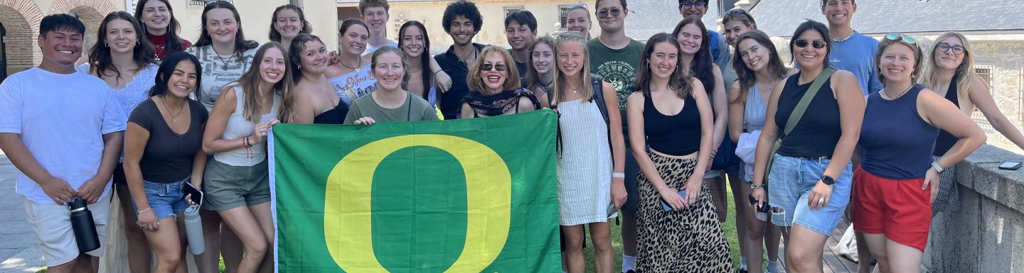 A group of university students and staff posing for a photo with one person in the front holding a green flag with a yellow O