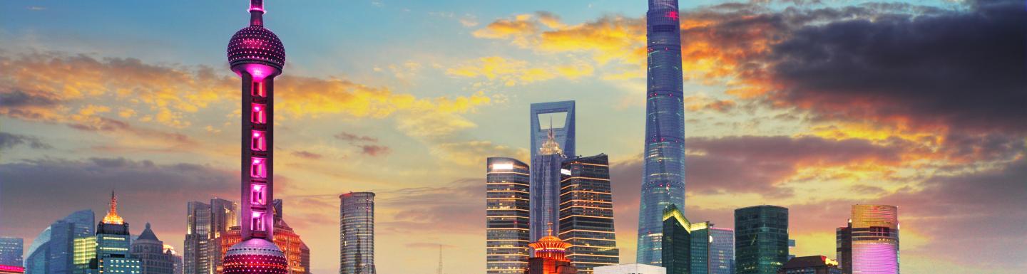 View of Shanghai city skyline at sunset with skyscrapers in background and body of water in foreground. 