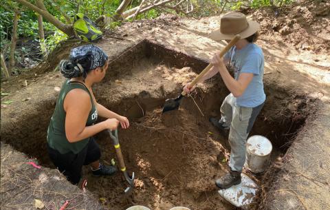 Link to UO Department Scholarships. Image Description: Two young women digging in a square hole