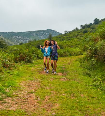 two college students with their arms around each other holding a peace sign while standing on a grassy hill