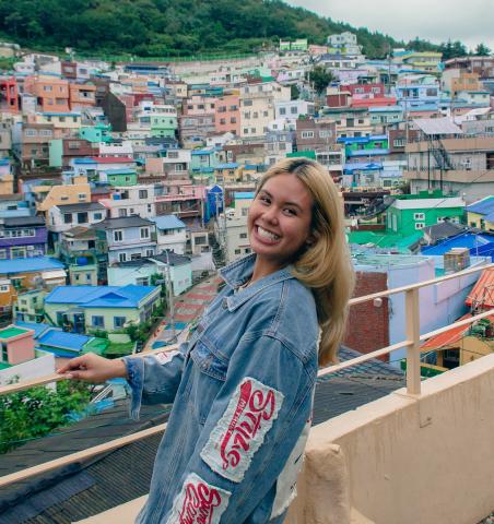 Young woman on a balcony with colorful house on a hill in the background