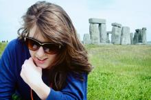 A young woman sitting in a grass field in front of Stonehenge