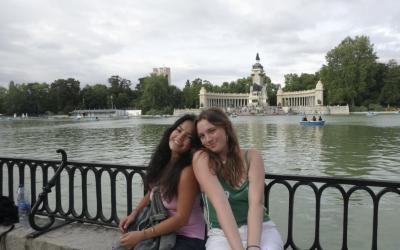 Two young women sit by a pond