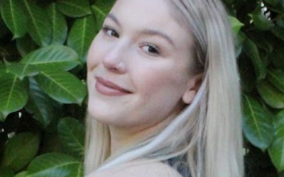 A young woman poses against a leafy background