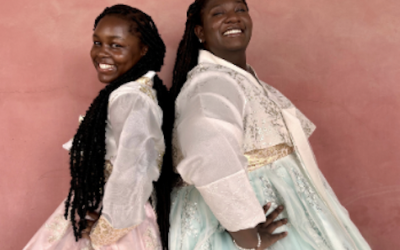 Two college students posing back-to-back wearing traditional Korean dresses.